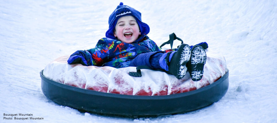 A little boy laughs as he slides down a snowy hill in a snow tube. 