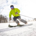 A man in a bright yellow-green ski jacket races downhill on skiis at Jiminy Peak Mountain Resort