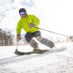 A man in a bright green jacket skis downhill while smiling at Jiminy Peak Mountain