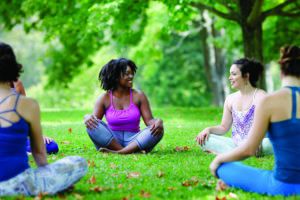 A group of women sit in a circle at an outdoor fitness class in summer