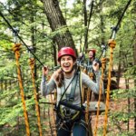 A woman stands with a happy look on her face among the ropes course at Ramblewild, which is nestled in the trees.
