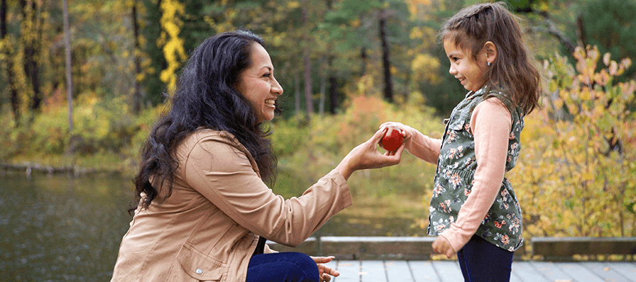 Woman hands child an apple on the dock at Pleasant Valley with a fall backdrop