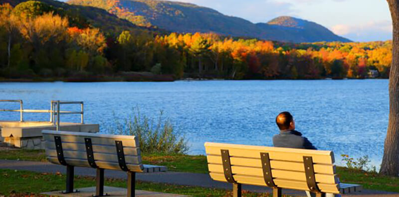 Man sits on bench viewing the fall foliage along Cheshire Lake