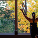 Woman displays yoga pose in front of window viewing fall foliage