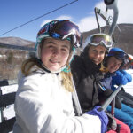 A family sits on a ski lift seat, traveling up the mountain at Jiminy Peak to ski.