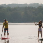 1B Summer 2023_4 Stockbridge Bowl_ paddle boarding_outdoor_water credit Great Sky Media 895×400 A father and daughter paddle board across the Stockbridge Bowl lake on a hazy summer day.