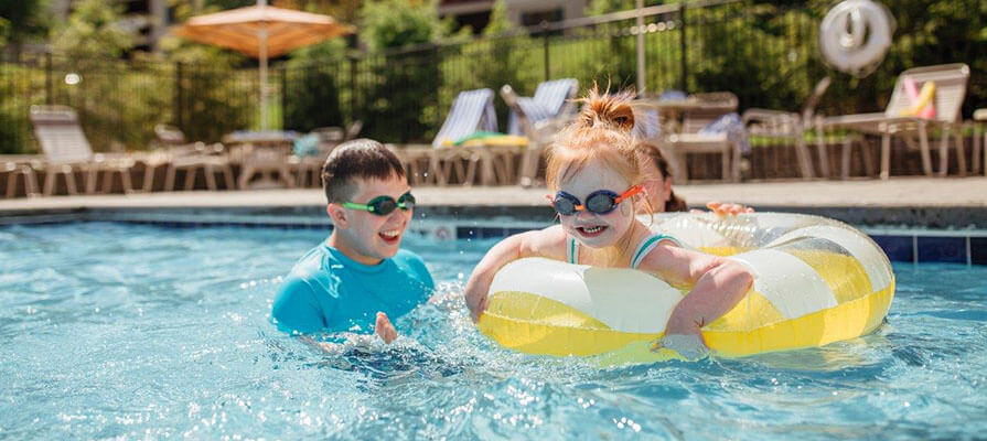 Two children swim and play in the pool at Oak and Spruce on a sunny summer day.