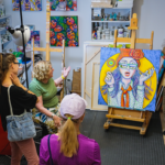 A group enjoys a collection of art at First Friday's Artswalk while the artist gives a discussion about the pieces