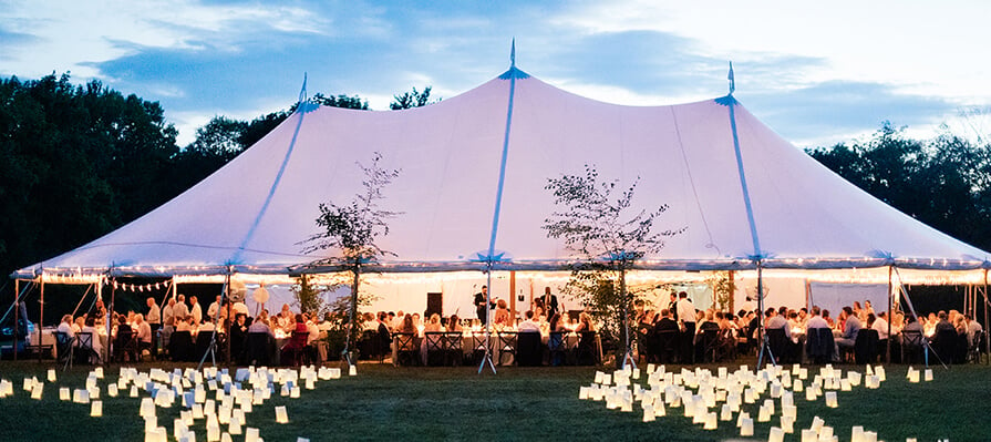 Outdoor canvas tent at dusk surrounded by hundreds of candles on the grass for a wedding reception