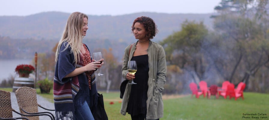 Two young women talk by a fire pit while they drink wine at Balerdash Cellars.