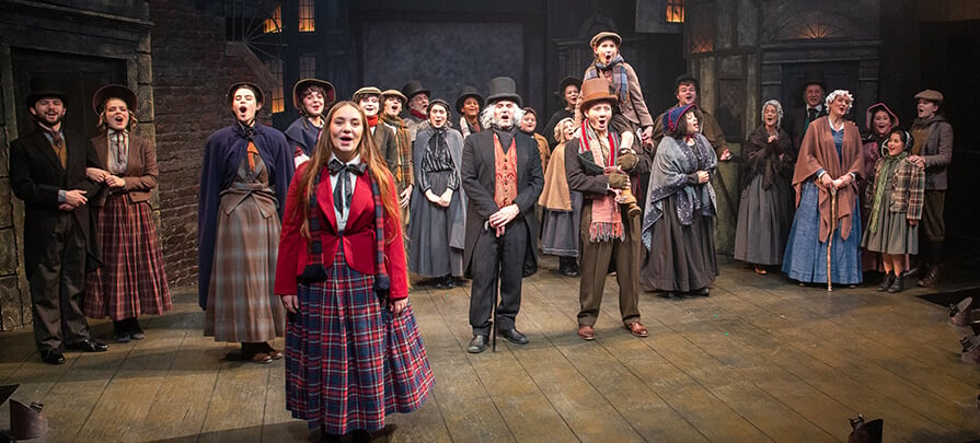 The cast of Christmas Carol at Berkshire Theatre Group stand across the stage singing an act all together as a large group.