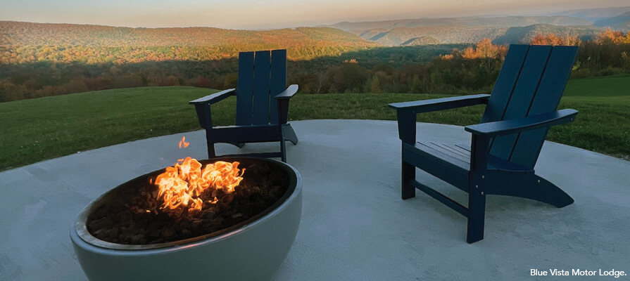 Two Adirondack chairs sit by a fire pit at Blue Vista Motor Lodge. In the background are the Berkshire mountains.