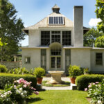 Chesterwood Studio is a white stone house with many glass windows. A fountain is in front in a green and flowery garden and lawn.