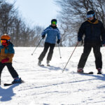 Two adults and a child ski down a snowy mountain