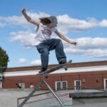 A person rides a skateboad over a jump at a skatepark on a sunny day.