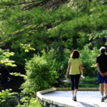 Two people stroll along the path at Pleasant Valley surrounded by green trees, grass, and water