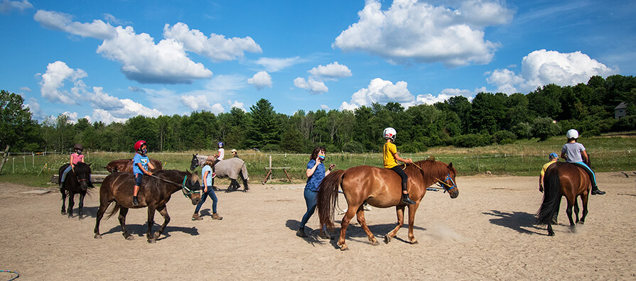 Children ride along horseback at Blue Rider Stables on a blue sky sunny day. 