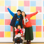 A family stands in front of a colorful art exhibit smiling at MASS MoCA