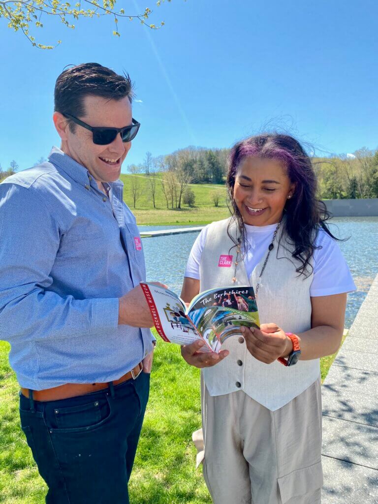 A man and a woman look at the Official Guide to the Berkshires booklet with smiles on their faces in the bright sunshine of the Clark Art.