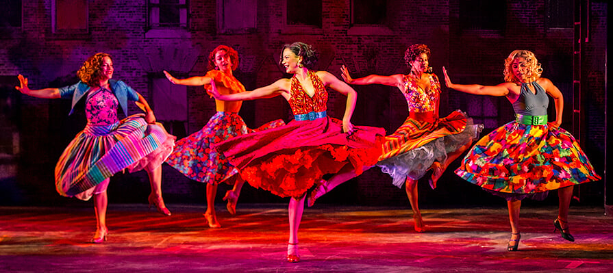 The company of five woman dance on the red lit center stage in flowing dresses during West Side Story. 