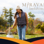 A woman of color dress for cool weather smiles as she places a rock on top of a rock sculpture at Miraval in the Berkshires.