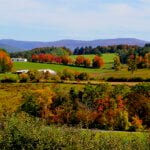 A rolling vista across fall foliage covered land with the mountains in the background.