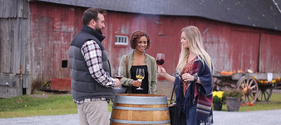 Three adults stand outside Balderdash Cellars savoring glasses of fresh local wine in the fall