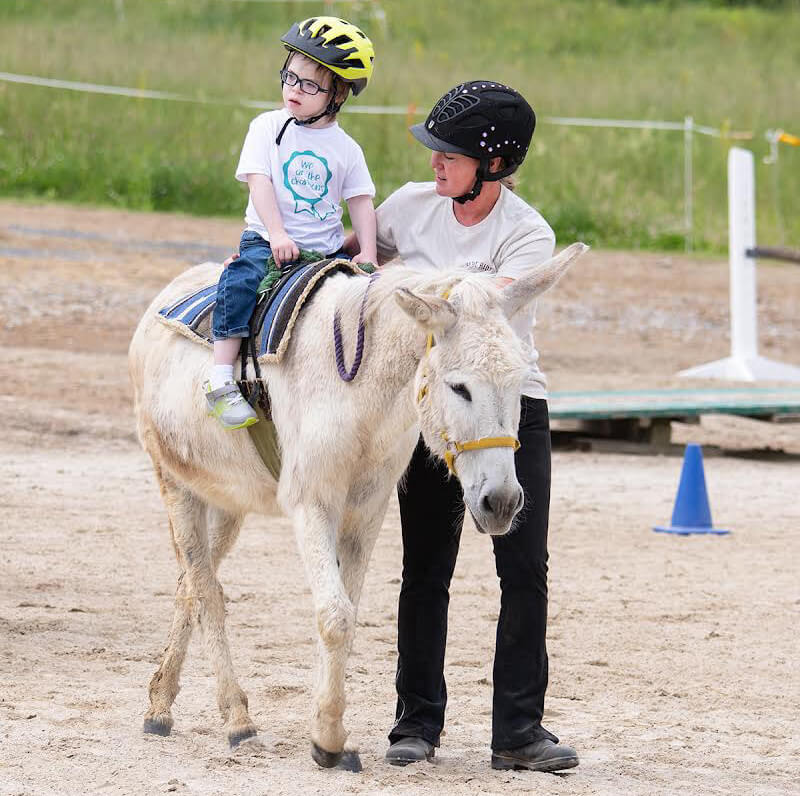 A young child rides horseback in a pen while a person walks alongside 