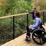 A woman in a wheelchair looks out over the foliage on the back deck with a young child