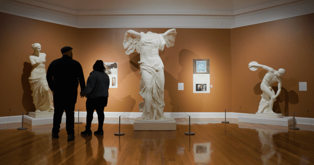 Winter 2024_Great Sky Berkshire Museum (3)_couple (2) A couple stands holding hands while looking at sculptures in the Berkshire Museum