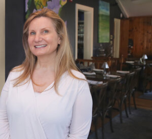 Colleen Taylor stands in front of several dining tables in her restaurant