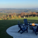 Blue Vista Motor Lodge_credit Cathleen King (2) 895×400 Four blue lounge chairs circle around a fire pit outside the Blue Vista Motor Lodge. In the background the trees and mountains filled with colorful foliage.