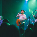 Mark Broussard sings with his band under colored spotlights