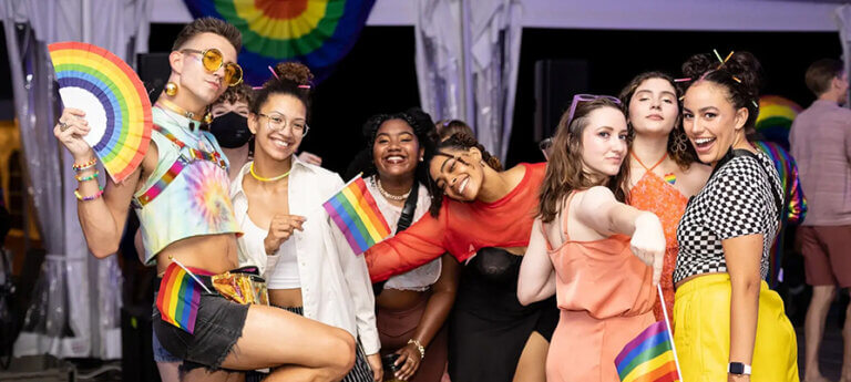 pillow-pride-25-895×400 A group of young adults pose while celebrating at Jacob's Pillow Pride, with Pride flags and accessories.