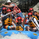 A group of adults sail down the river as they whitewater raft the rapids.