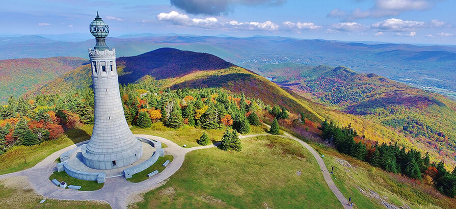 An aerial view of the Mount Greylock war memorial tower surrounded by foliage in fall