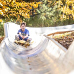 A young boy laughs as he rides the alpine slide through the foliage