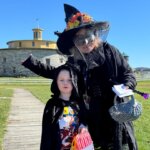 an adult and child smile for a photo in full costume for halloween in front of Hancock Shaker Village