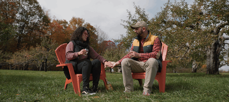 p58 2022 FALL_Great Sky Media_4 – Hilltop (1) 895×400 A couple holds hands as they sip cider in a fall apple orchard