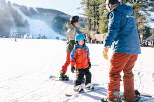 A child and two adults coast on the snowy mountain of Berkshire East while snowboarding