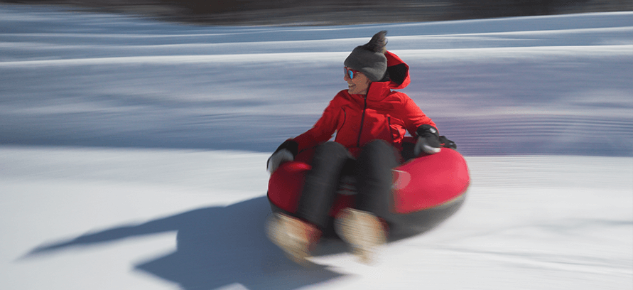 A woman in red slides down a snowy mountain on a red tube at Ski Butternut. 