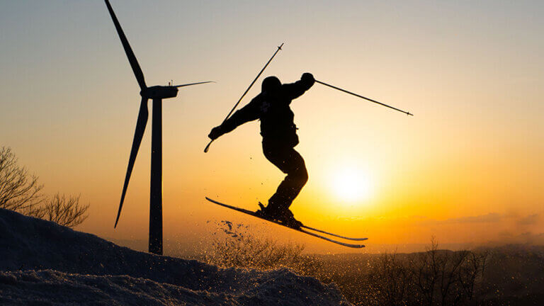 A skier poses mid-air while jumping on the slopes of Jiminy Peak at sunset