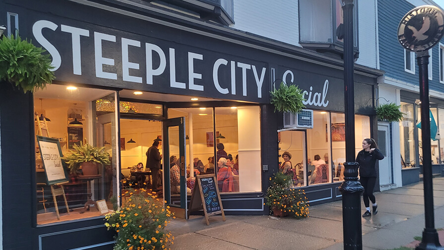 Steeple City Social gathering spot is full with customers sitting at tables as we are looking in through the windows