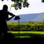 A violinist plays on the open air lawn of Tanglwood with the Berkshire mountain range in the background