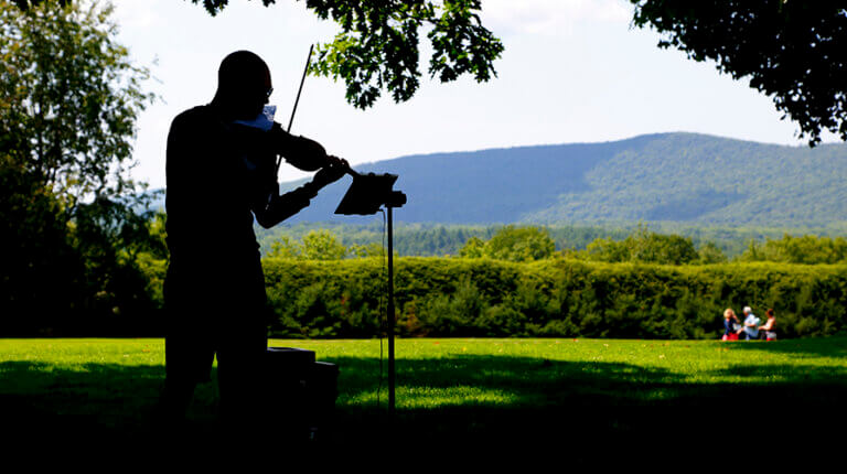 A violinist plays on the open air lawn of Tanglwood with the Berkshire mountain range in the background