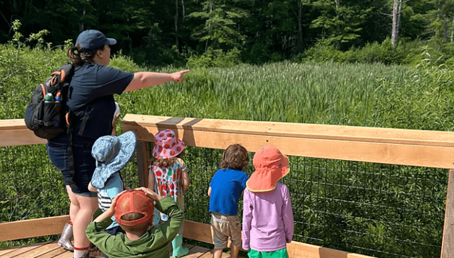 A group of young children and an adult look out into the Pleasant Valley greenery
